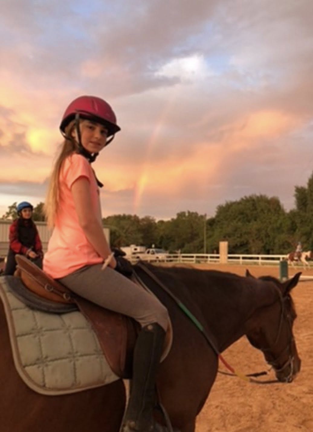 Young rider enjoying sunset horseback ride with rainbow
